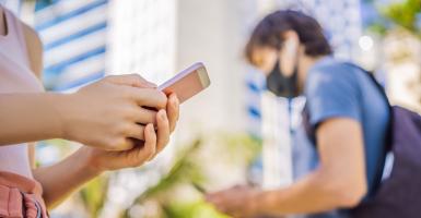 Un homme masqué et une femme en rue qui regardent leur smartphone