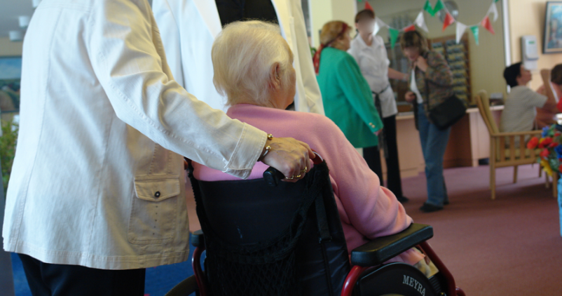 Personne senior poussée sur une chaise roulante dans une maison de repos