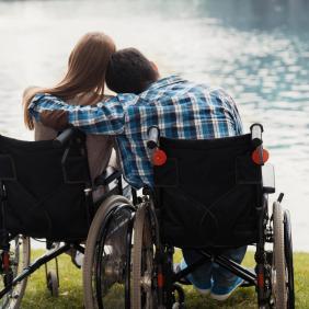 Un couple en chaise roulante de dos, se tenant affectueusement dans les bras l'un de l'autre